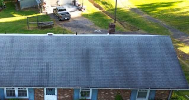 Drone view of a brick ranch house with an old, stained gray shingle roof.