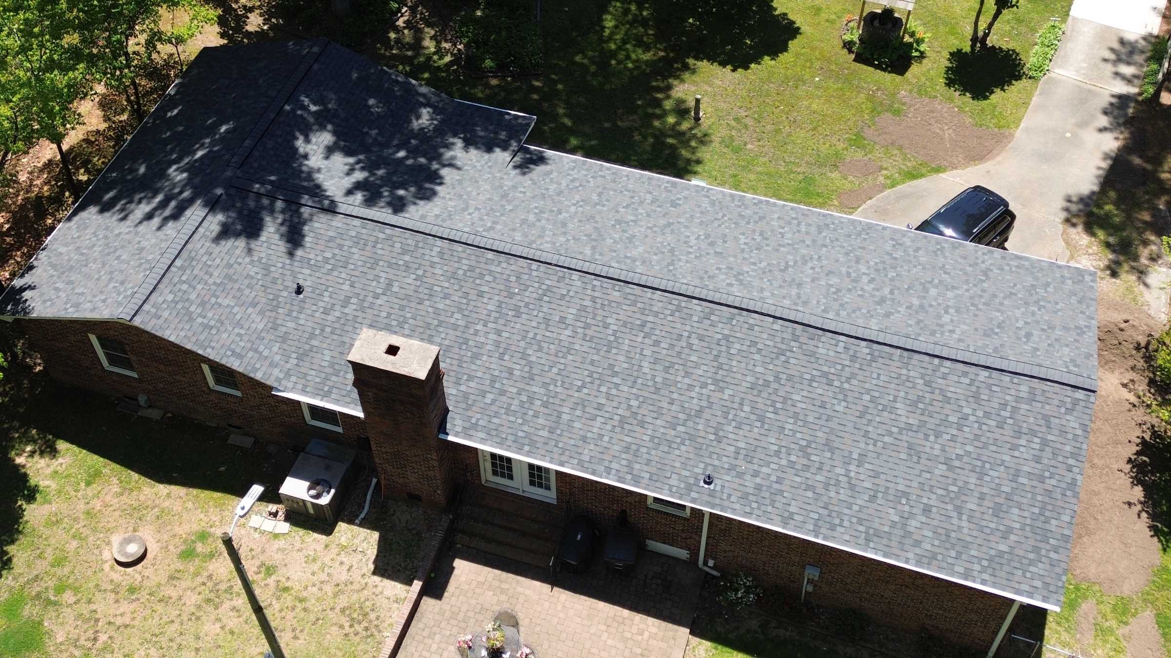 Drone view of a long brick ranch house with a new gray shingle roof.