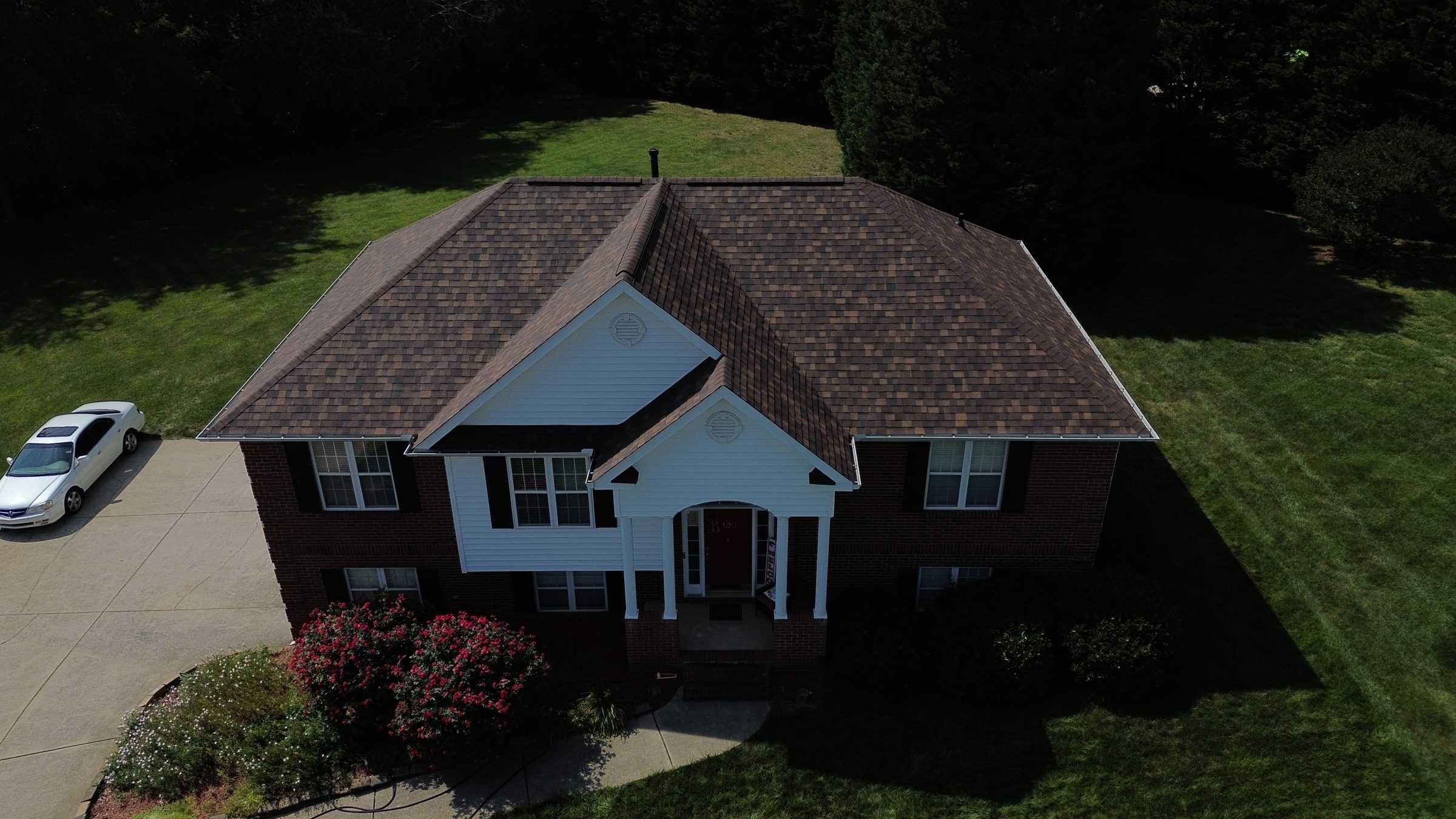 Drone view of a brick two-story house with a new brown shingle roof.