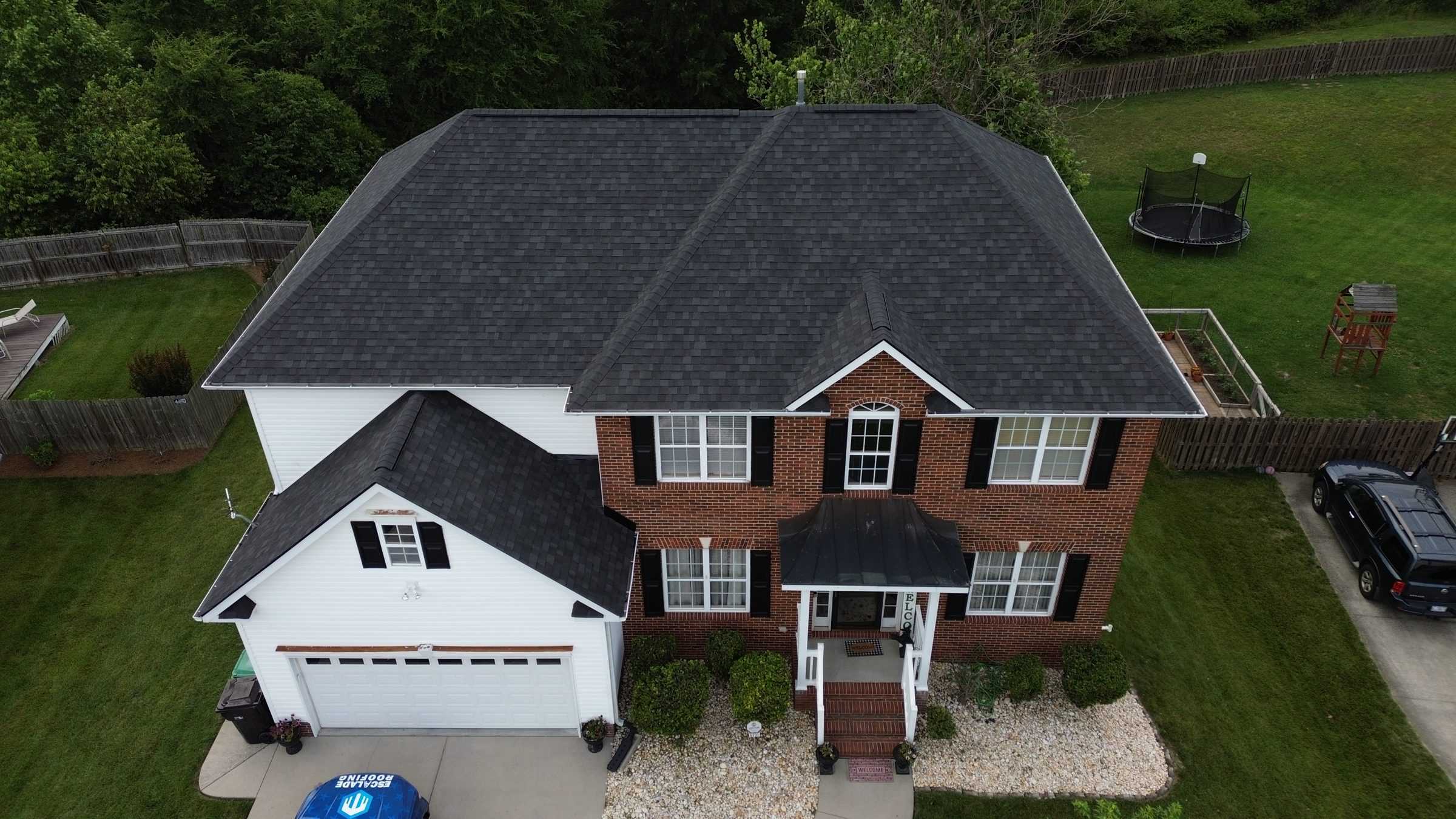 Drone view of a brick and white two-story house with a new charcoal roof.